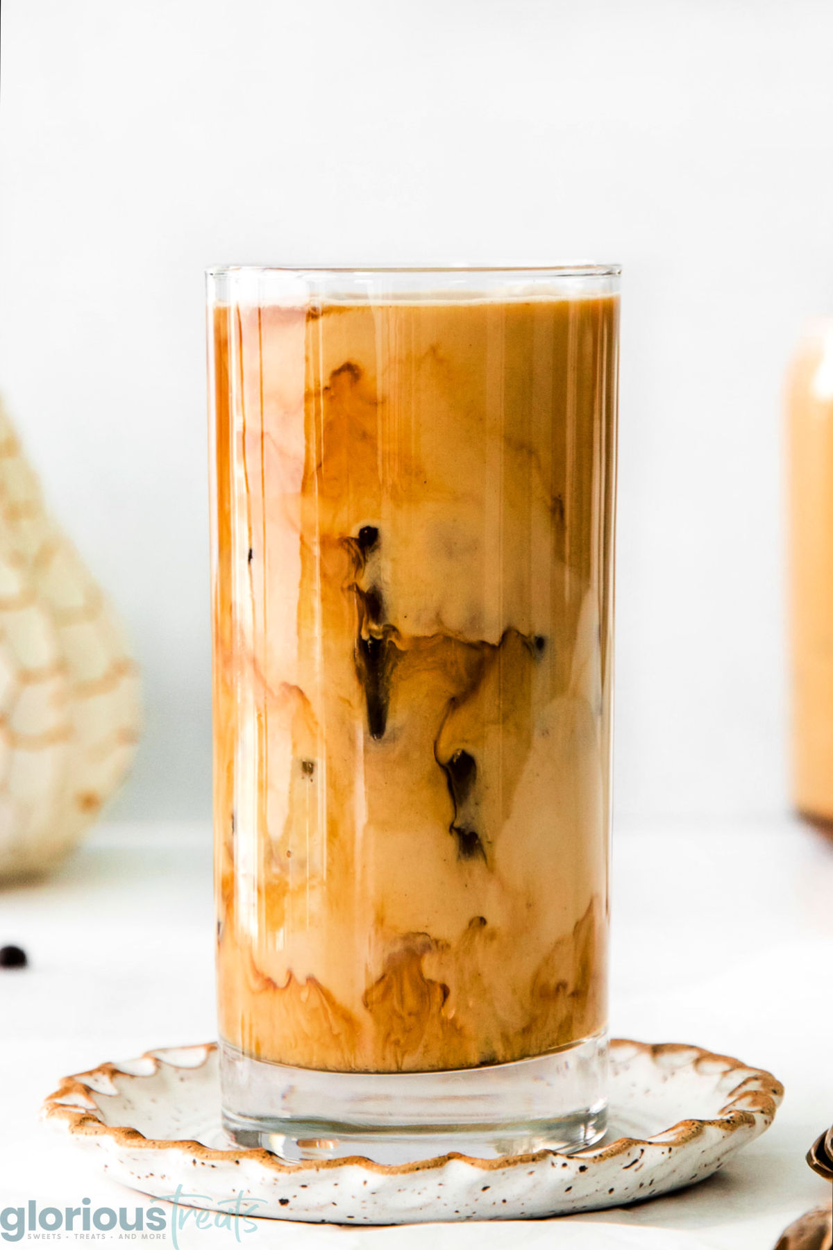 A side view of a glass of pumpkin cream cold brew on a decorative plate.