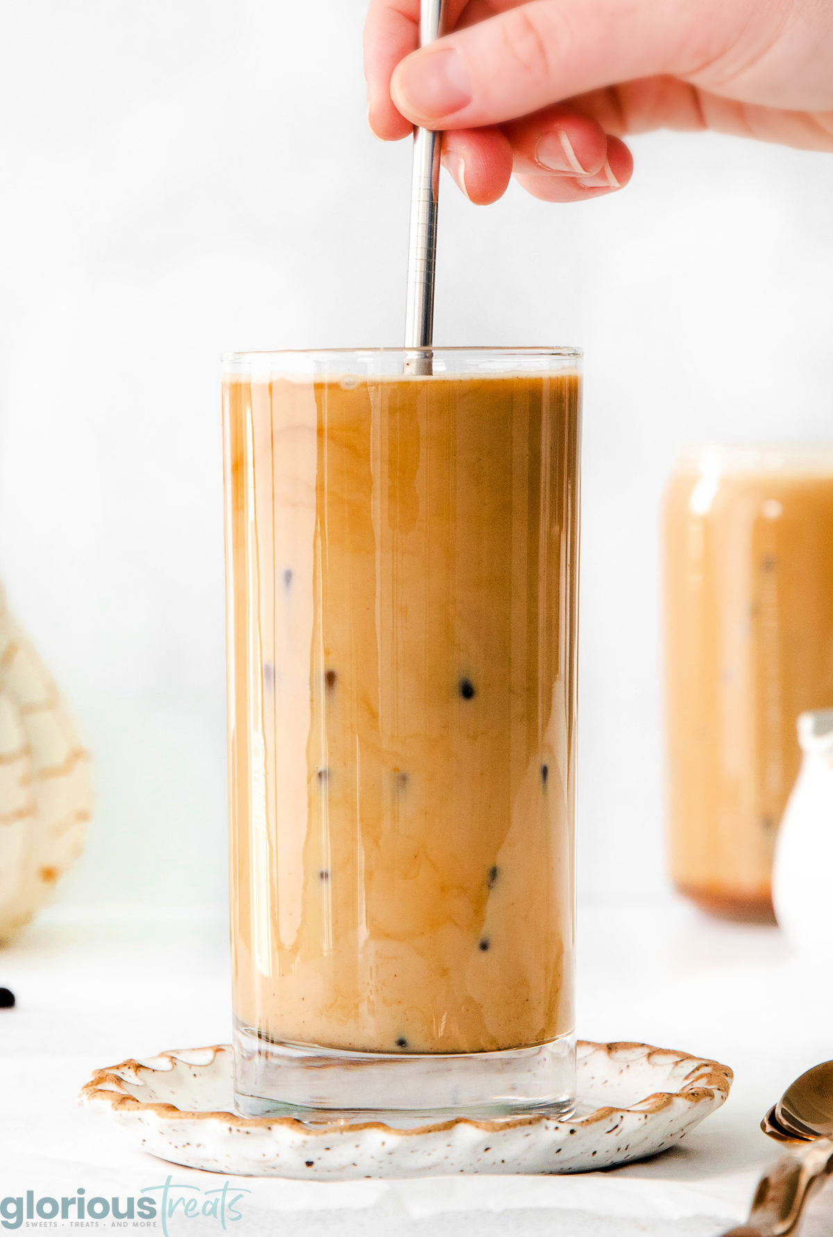 A hand holding a metal straw in a glass of pumpkin cream cold brew. The glass is on a decorative plate.