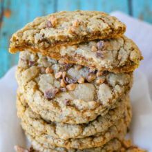 Toffee cookies stacked high on a square white plate. Top cookie has been broken in half to show the chewy interior.