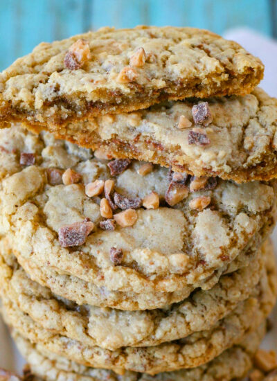 Toffee cookies stacked high on a square white plate. Top cookie has been broken in half to show the chewy interior.