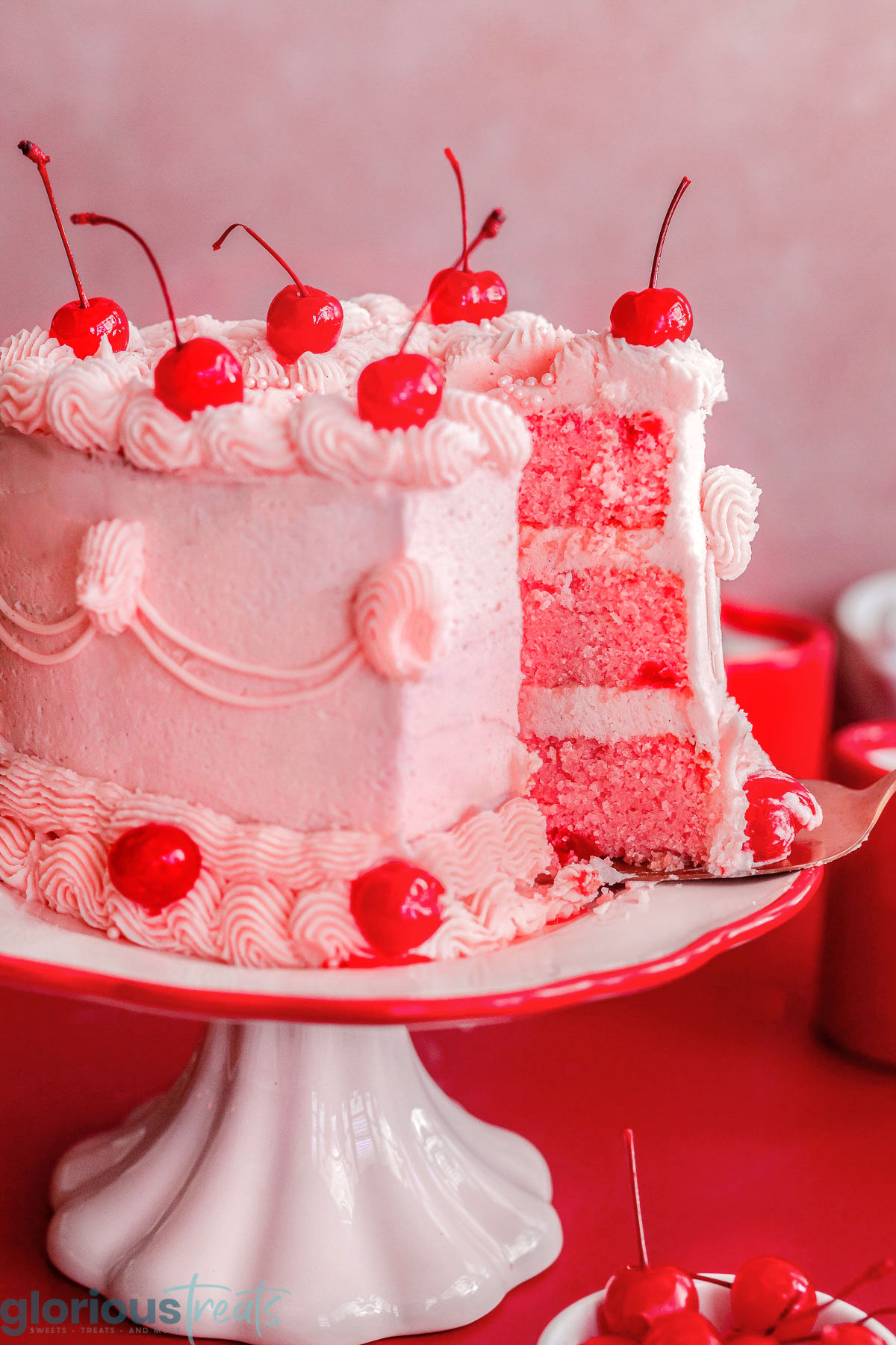 Piece of cherry cake being pulled away from the rest of the heart shaped cake on the cake stand.