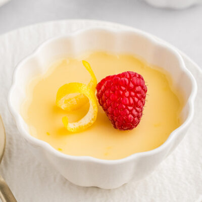 A close up view of lemon posset in a white decorative bowl on a plate. More posset is in the background.