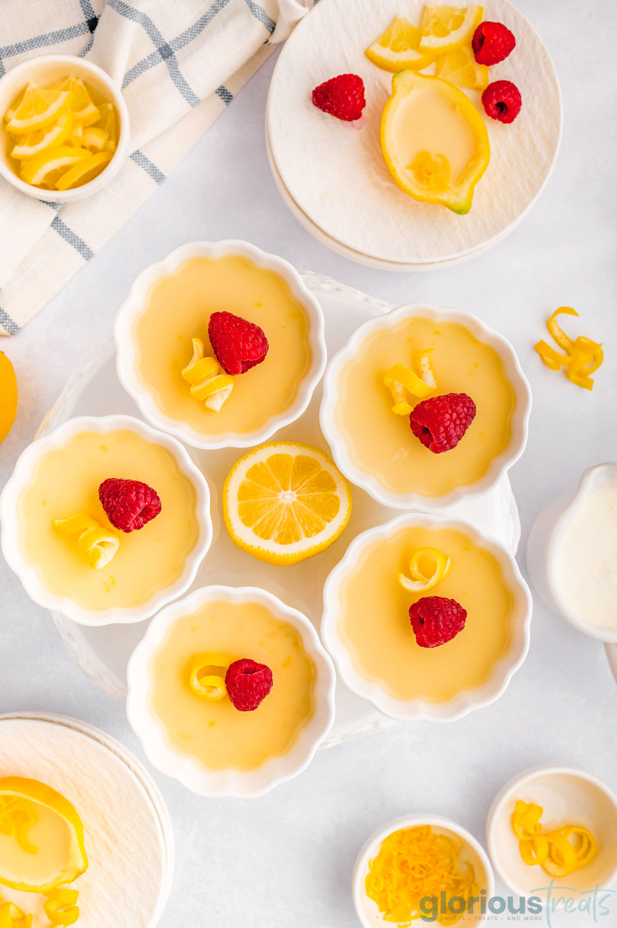 5 Lemon Posset in decorative white bowls. Toppings are placed around the bowls.